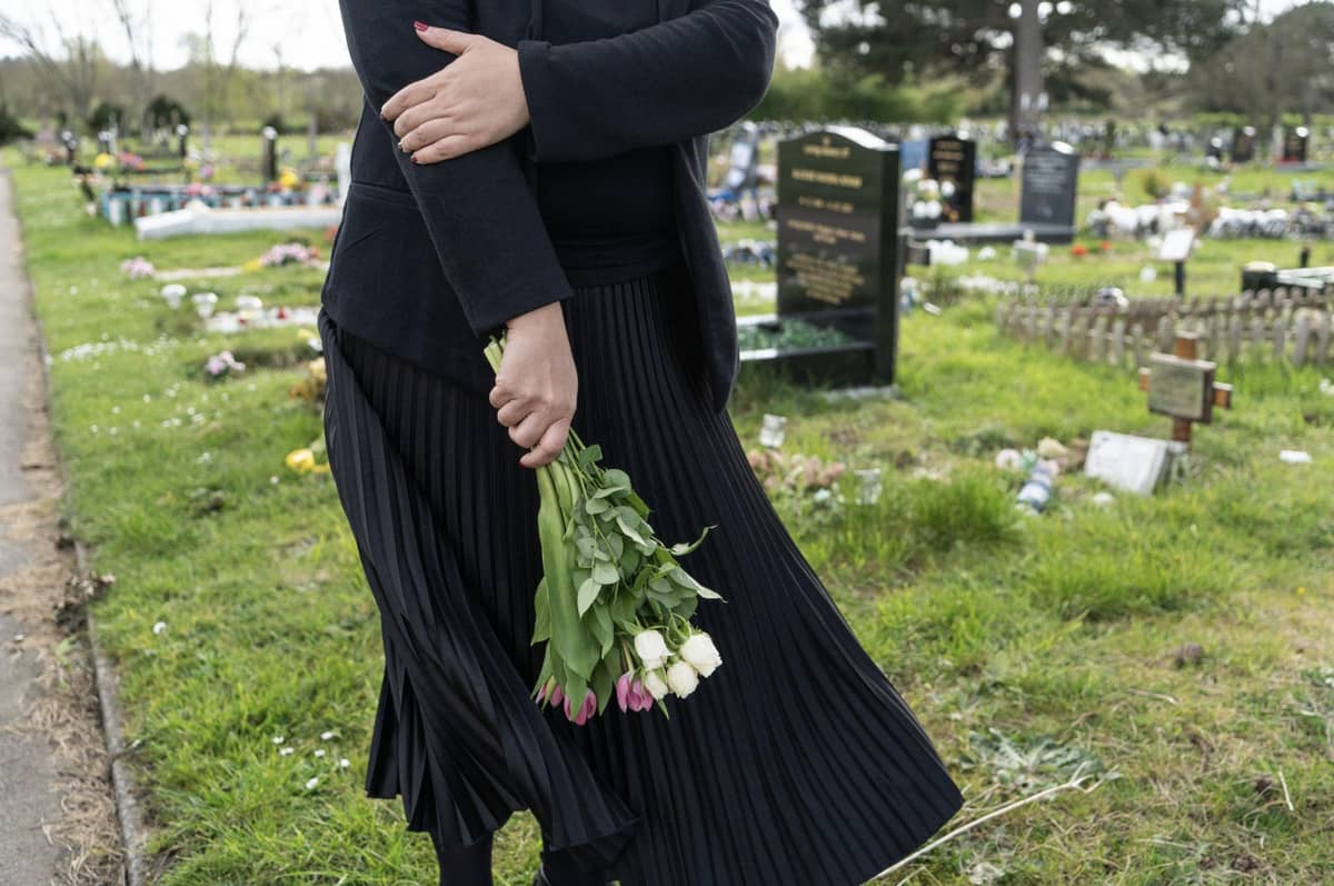 Women dressed in black at a tombstone carrying flowers