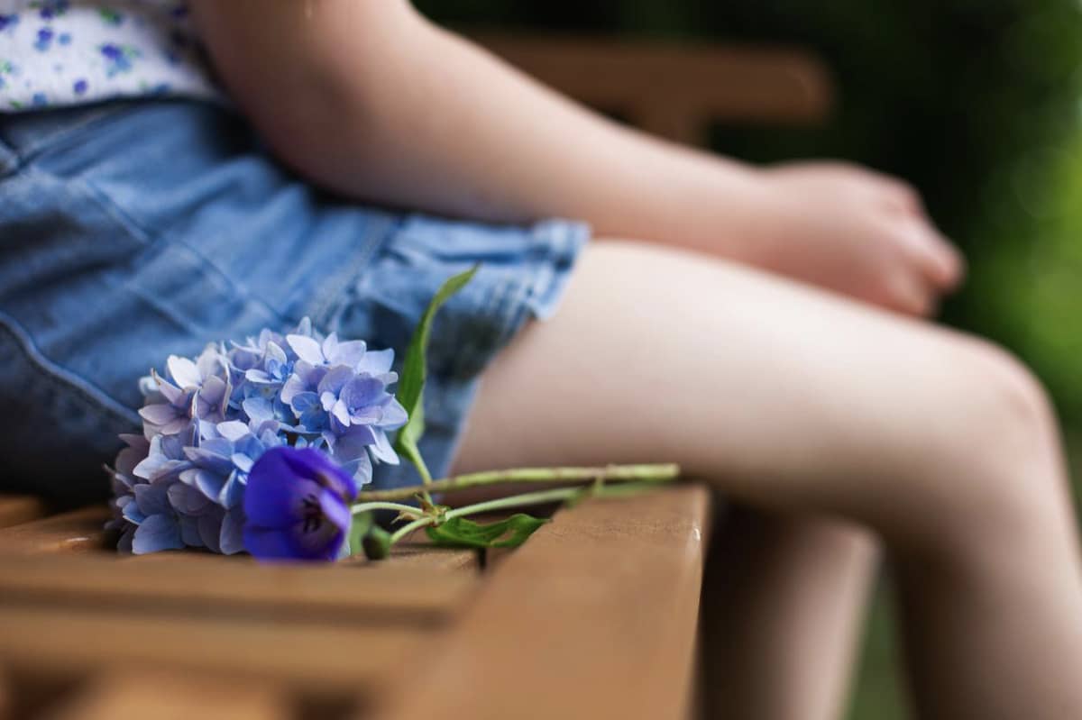 A child sitting on a bench with a flower beside them